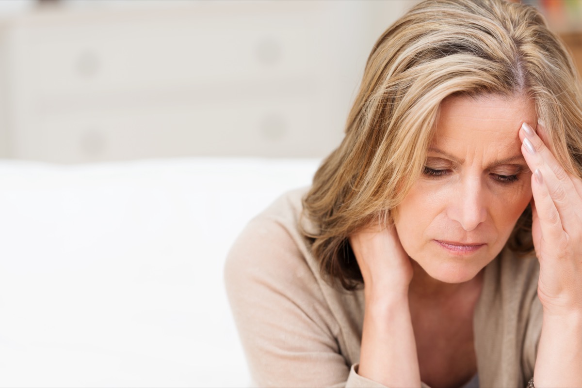Woman suffering from stress or a headache grimacing in pain as she holds the back of her neck with her other hand to her temple.