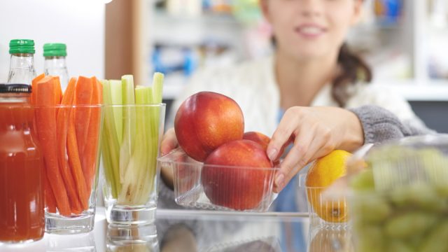 Woman reorganizing her fridge to put fresh fruits vegetables healthy snacks in front