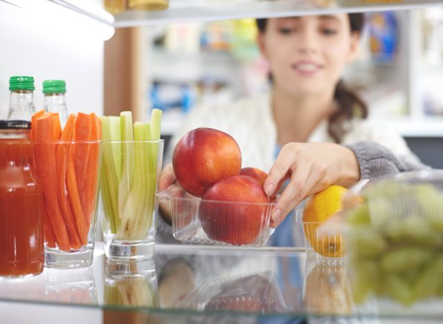 Woman reorganizing her fridge to put fresh fruits vegetables healthy snacks in front