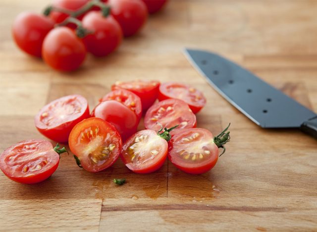 halved cherry tomatoes with knife on cutting board