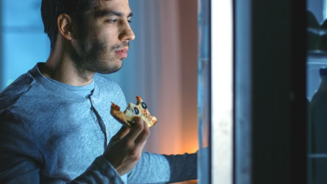 man eating leftover pizza as a late night snack