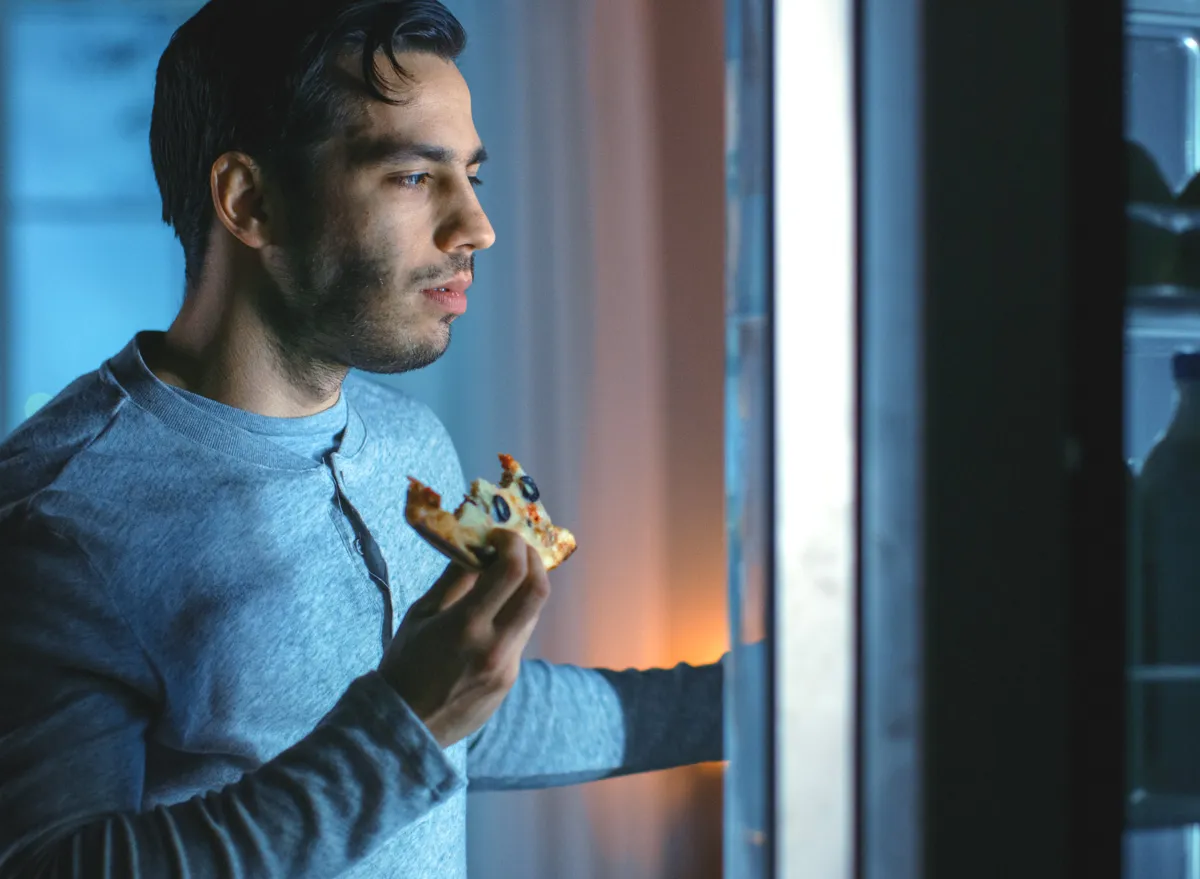 man eating leftover pizza as a late night snack