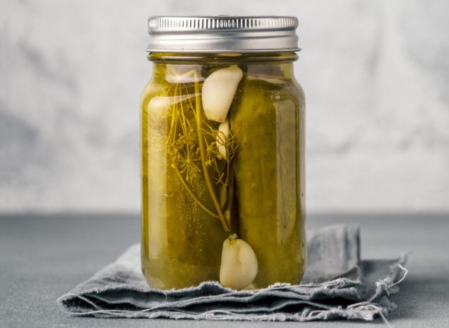 New pickled cucumbers in glass jar with herbs and garlic