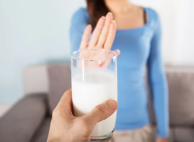 Woman holding up an outstretched hand and saying no to a man offering her a glass of milk