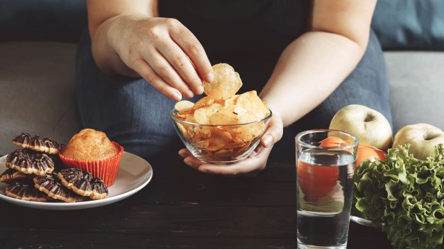 Woman choosing to eat junk food chips instead of swapping for healthy vegetables