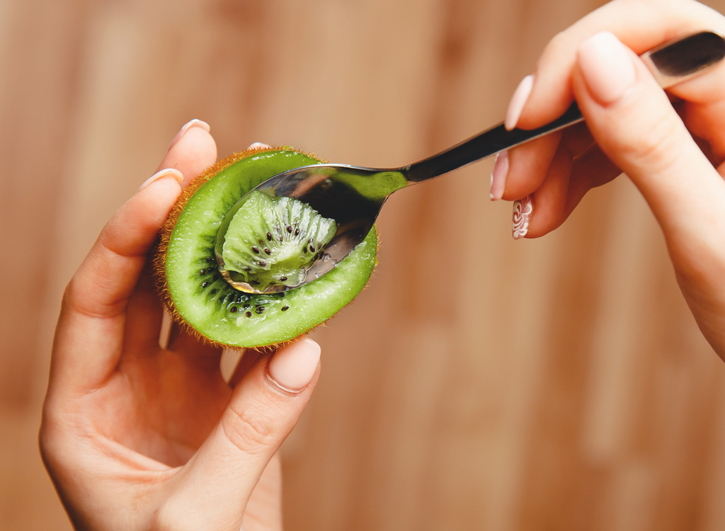 Woman using spoon to eat kiwi