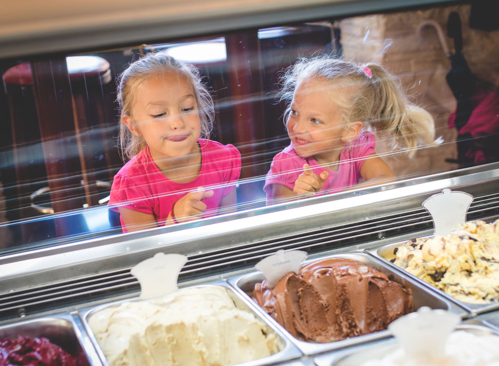 Girls touching glass in front of ice cream counter