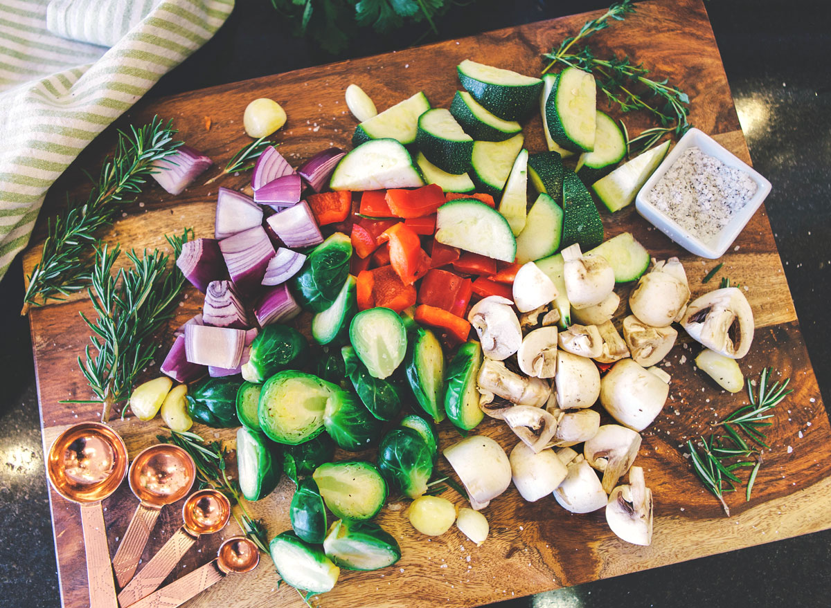 Meal prep chopped veggies brussels sprouts onions mushrooms peppers zucchini on wooden cutting board