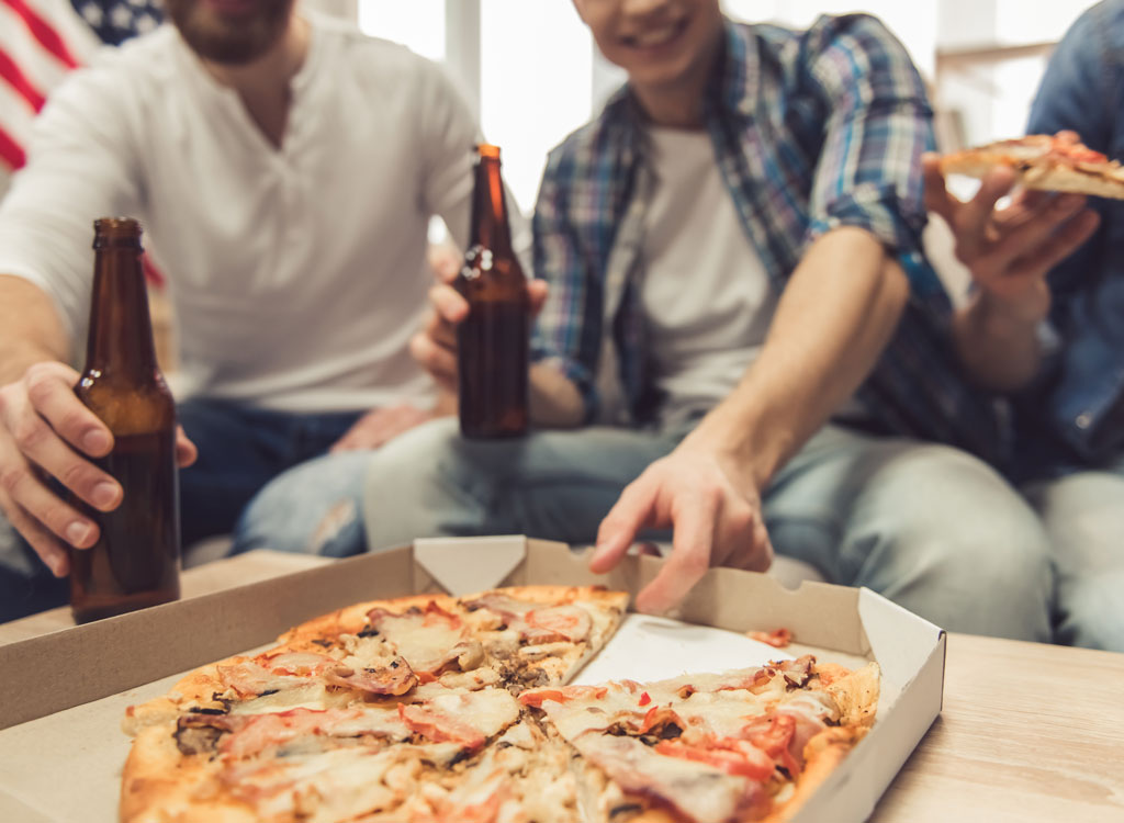 Man holding beer reaching for slice of pizza