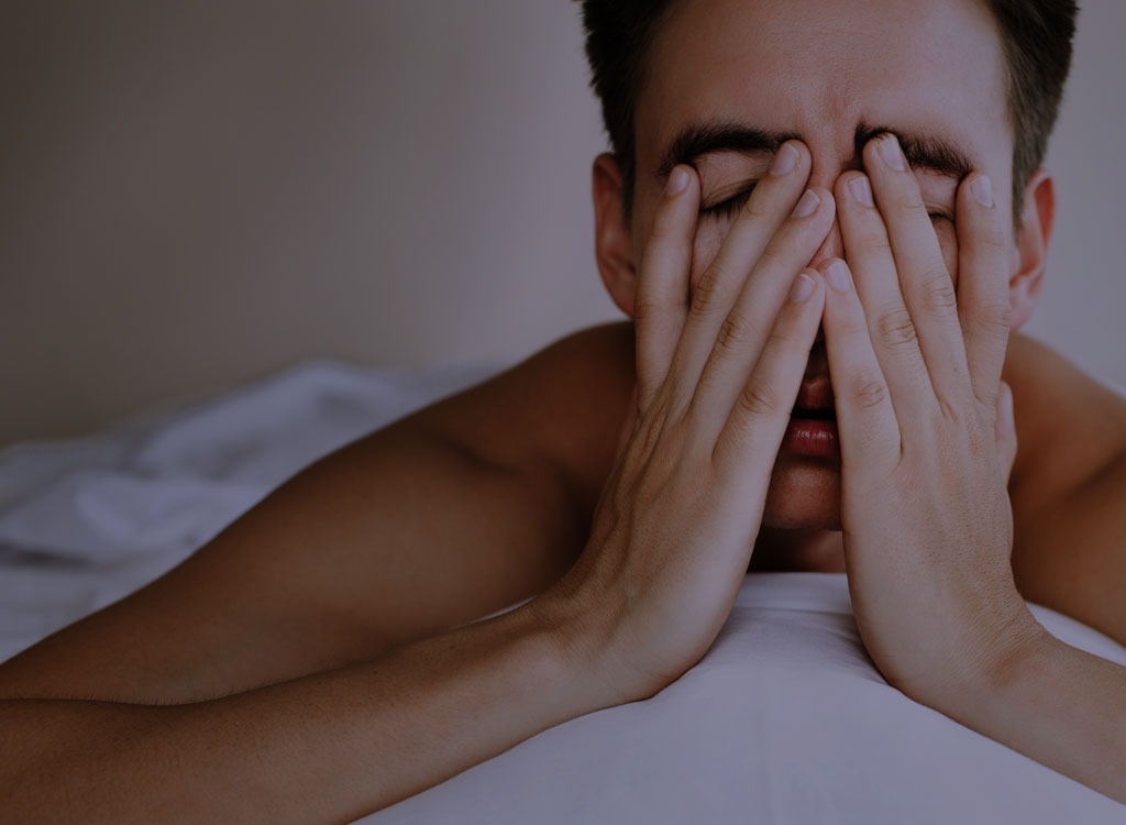 Man with hands over face in bed