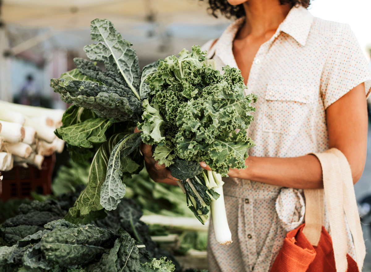 Woman picking out kale and leeks at a farmers market or grocery store