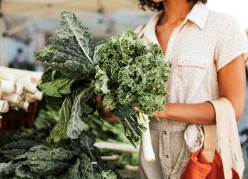 Woman picking out kale and leeks at a farmers market or grocery store