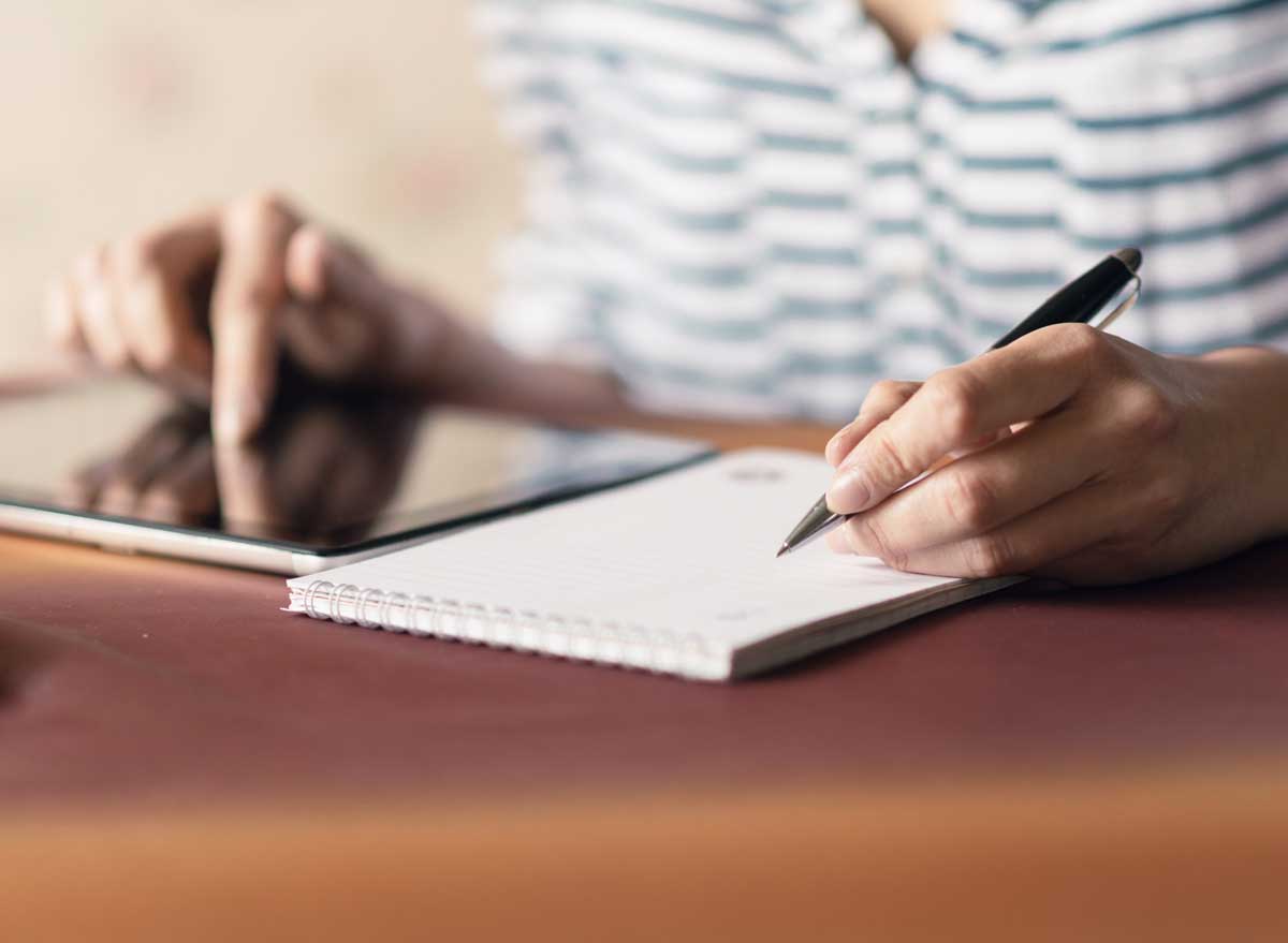 Man writing a to do list while also on his tablet computer