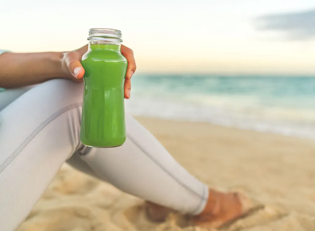 Woman holding green juice beach