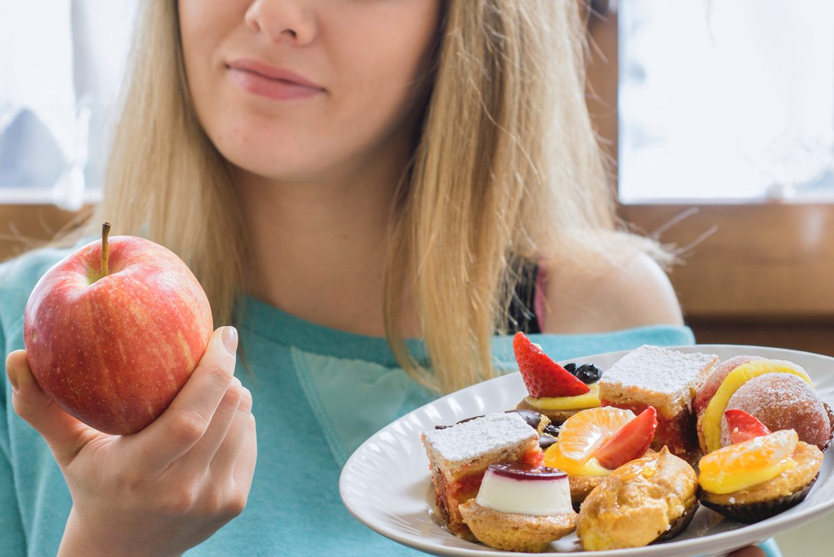 woman choosing healthy apple instead of junk dessert as a food swap to cut calories