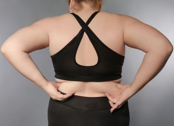 woman in sports bra touching back fat