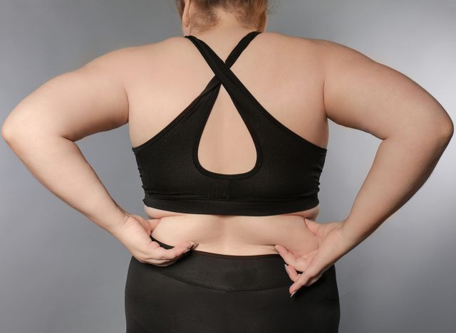 woman in sports bra touching back fat