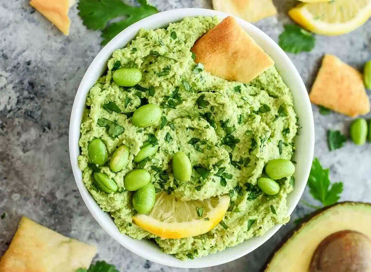 edamame avocado hummus in serving dish with pita chips, lemon slice, and avocado half