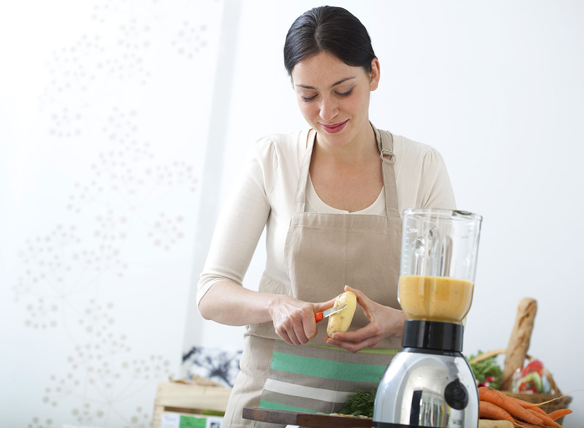 woman peeling potato for soup in blender