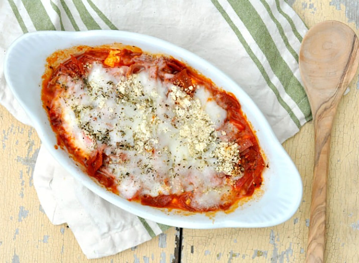 microwave pizza dip in white baker with striped dish towel and wooden spoon