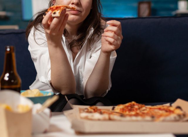 woman overeating bingeing on pizza and beer while watching tv