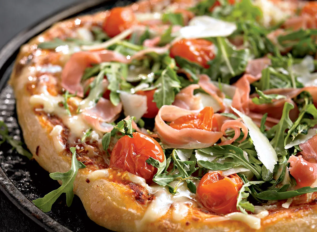 Healthy pizza with arugula, cherry tomatoes, and prosciutto