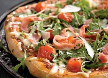 Healthy pizza with arugula, cherry tomatoes, and prosciutto