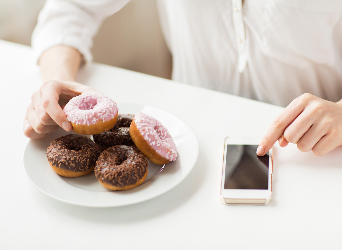 A woman counting calories on her phone for an unhealthy dessert donut