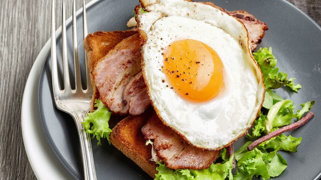 Fried egg on a blt sandwich on gray plate with fork