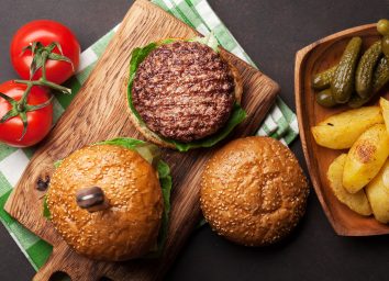 open-faced burger on wooden cutting board with tomatoes and pickles on the side