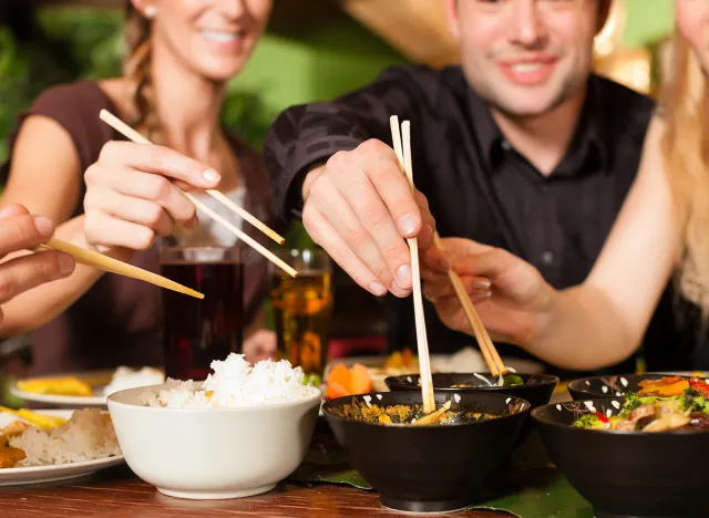 people eating thai and chinese food with chopsticks at a table