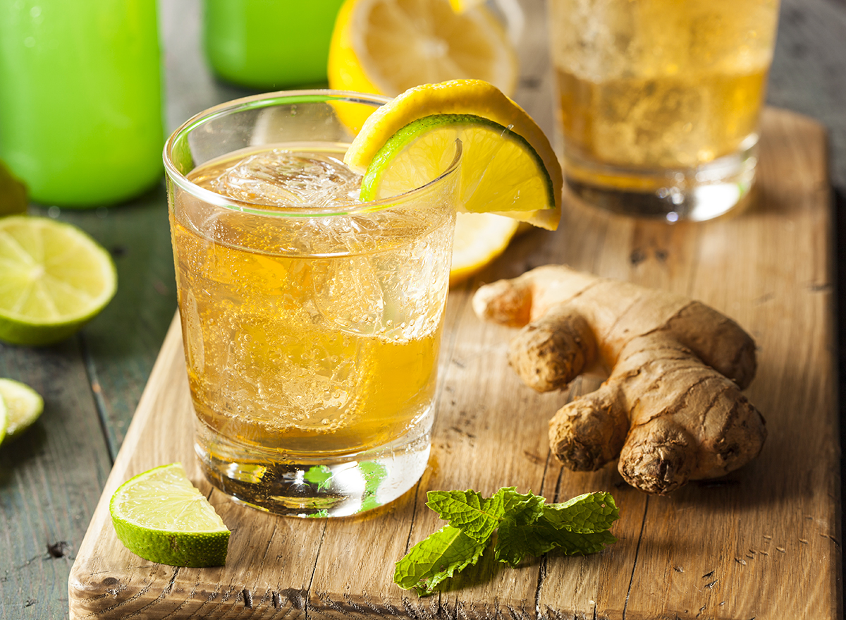 glass of ginger ale on wooden cutting board with ginger root lemon lime and mint leaves
