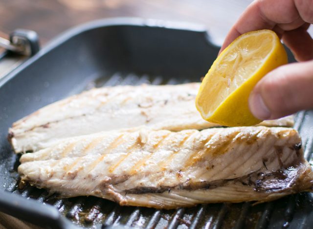 Grilled mackerel on grill pan squeezing lemon juice by hand