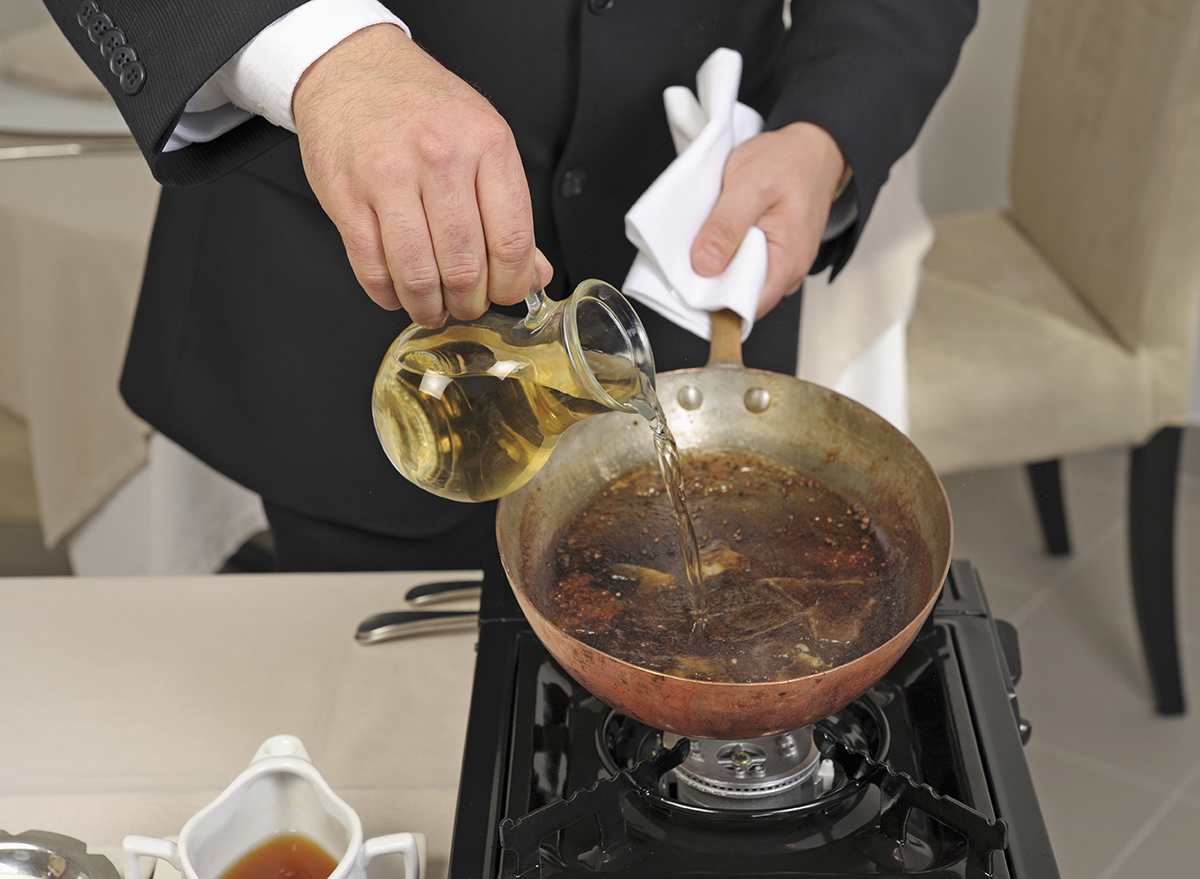 person wearing a suit deglazes a pan over a stovetop