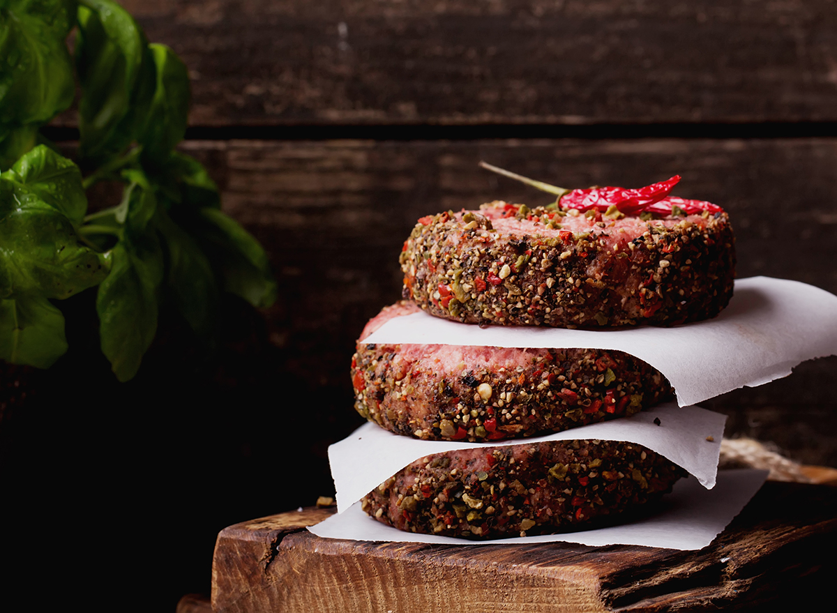 three raw seasoned burger patties stacked on top of one another