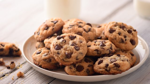 chocolate chip cookies on a plate with two cups of milk in the background