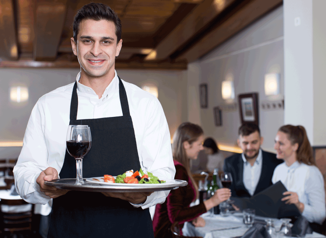 waiter with drinks and salad on tray standing near table