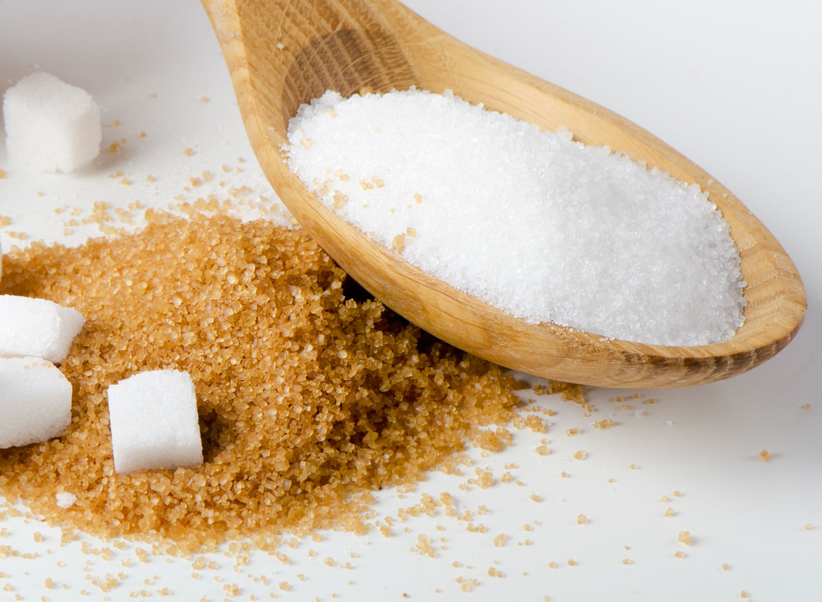 White sugar in wooden spoon resting on brown sugar