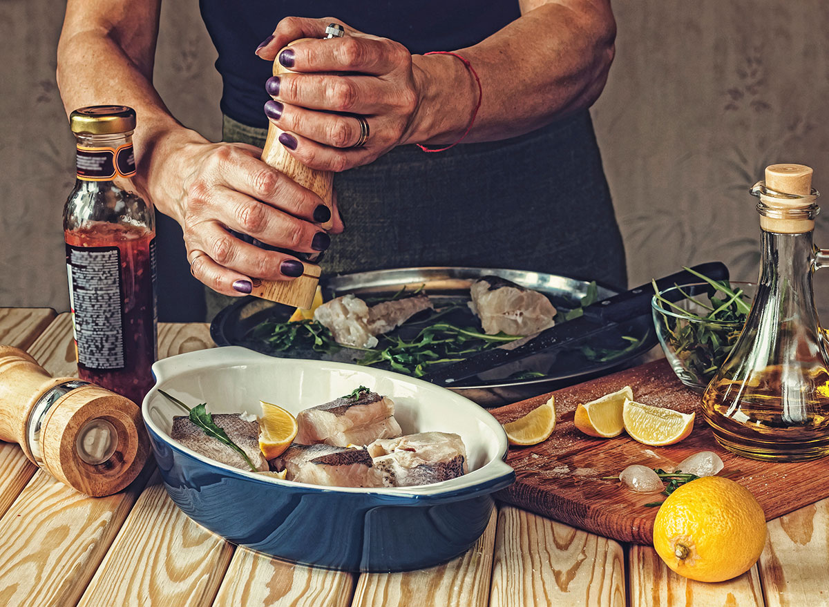 woman seasoning fish in a pan with olive oil lemon and salt