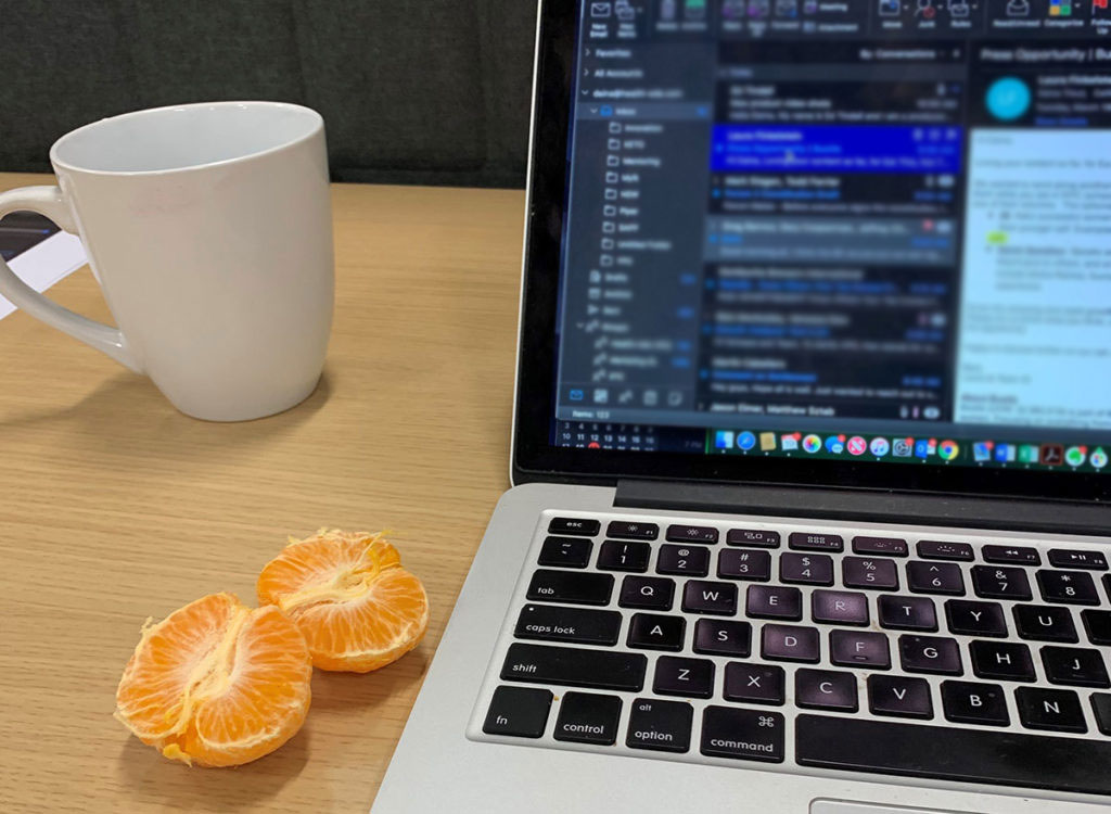 glass mug of water with tangerine next to laptop