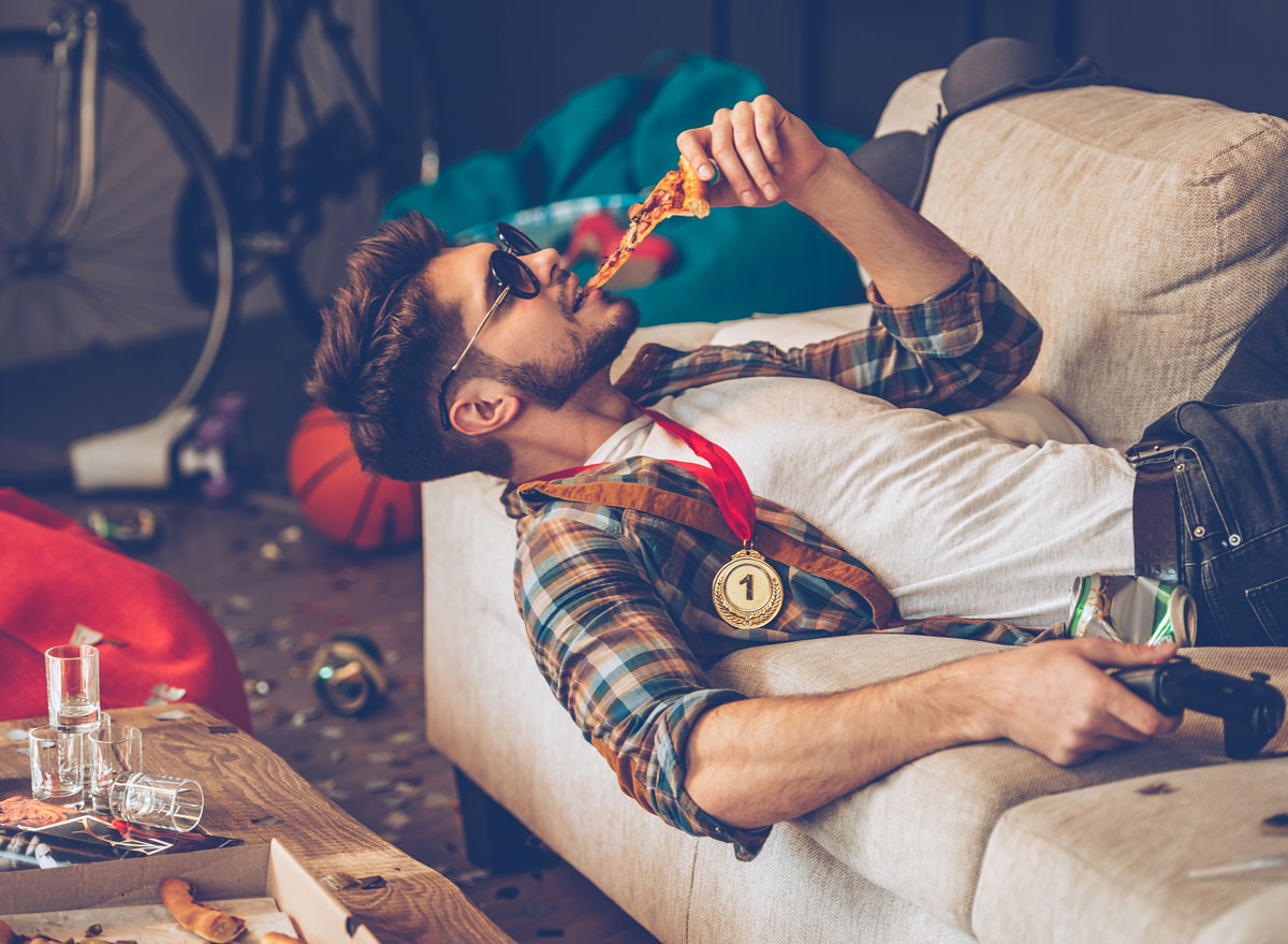 drunk man eating pizza on couch in messy room