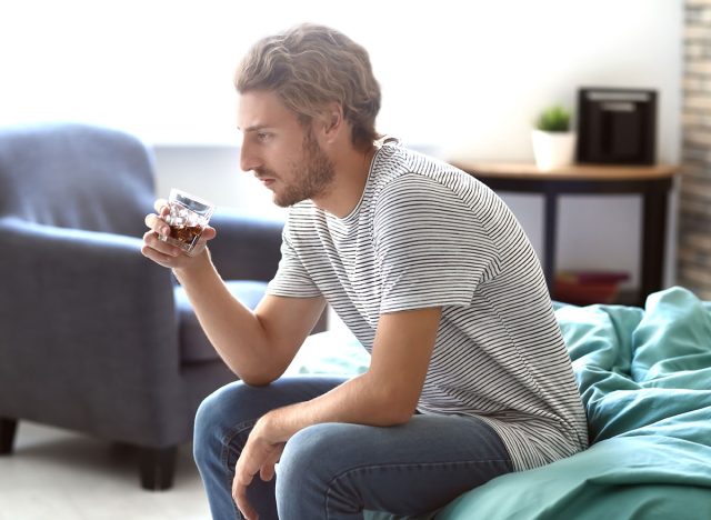 man sitting on bed with alcohol glass - how does alcohol affect the brain