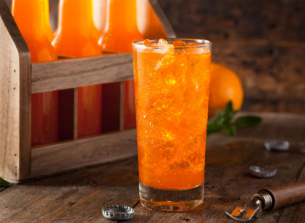 glass of orange soda with bottles in background