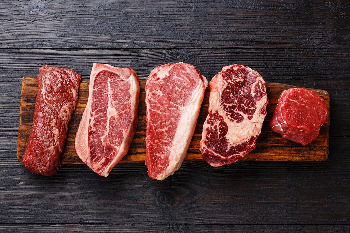 slabs of different cuts of red meat on wooden cutting board