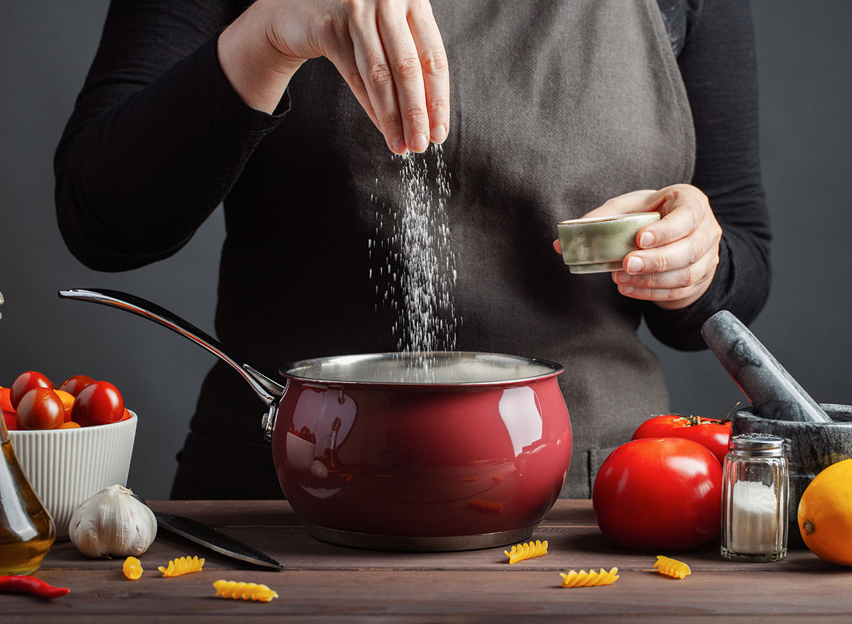 hands adding salt to pasta water