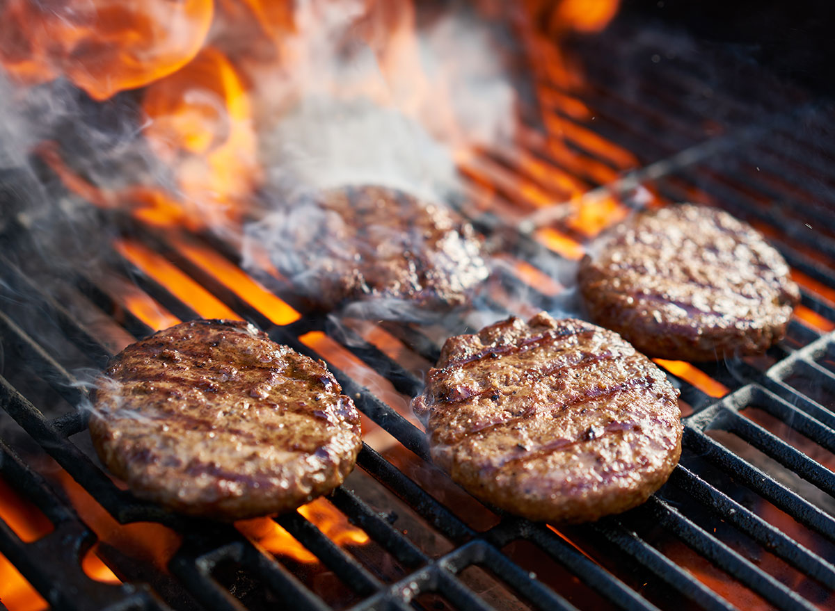 flames behind cooking burger patties