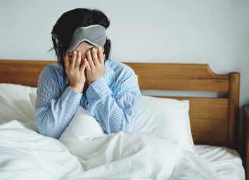 Woman waking up in bed but is exhausted and sleep deprived