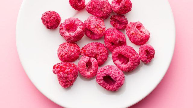 freeze dried raspberries on white plate pink background