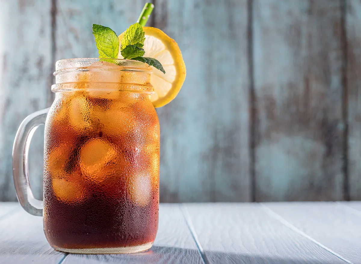 iced tea in a mason jar with a green straw, lemon wheel, and a sprig of mint