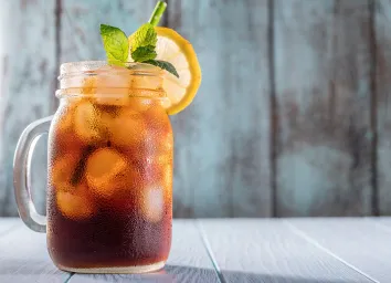 iced tea in a mason jar with a green straw, lemon wheel, and a sprig of mint